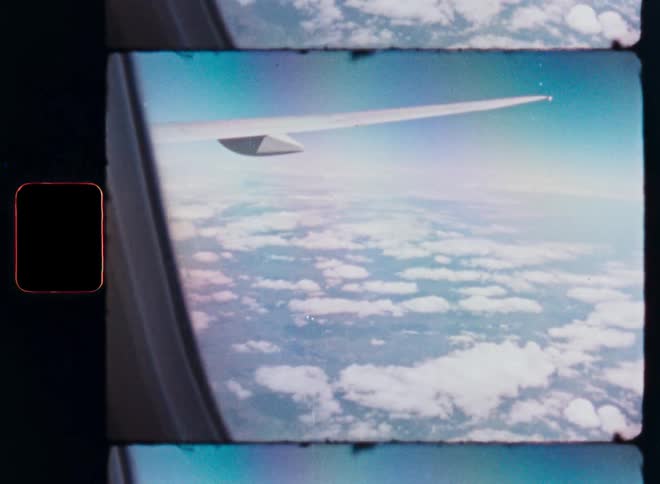 A dreamy vintage 8mm film captures the view from an airplane window, looking out over a sea of clouds as the wing comes into sight