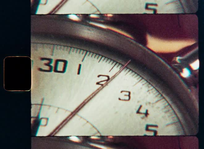 A vintage stopwatch ticks away the seconds in an extreme close-up shot on grainy Super 8 film