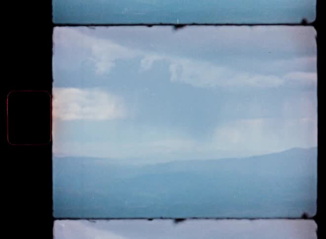 Vintage Super 8 footage shows a distant rainstorm passing over hazy blue mountains under a cloudy sky