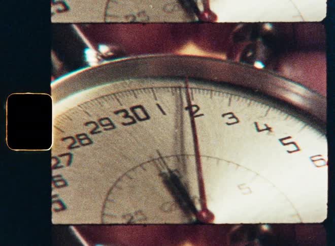 A vintage 8mm film strip captures a close-up of a running analog stopwatch as the second hand ticks by