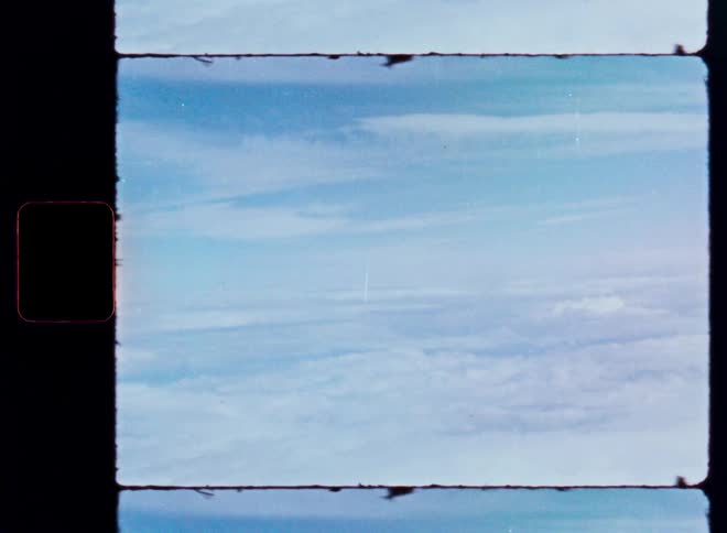 An archival 8mm film scan shows a peaceful view of the blue sky and white clouds from above