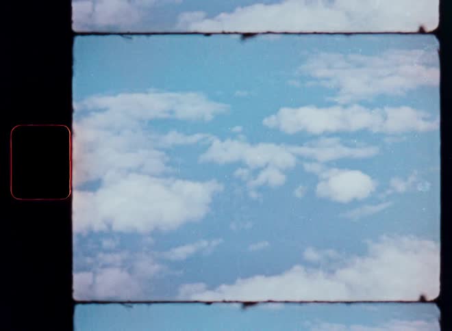 A vintage 8mm film captures a dreamy view of white fluffy clouds moving slowly across a blue sky