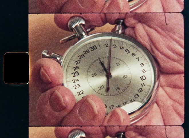 A close-up of a hand holding a vintage stopwatch as the second hand ticks by, captured on grainy retro film