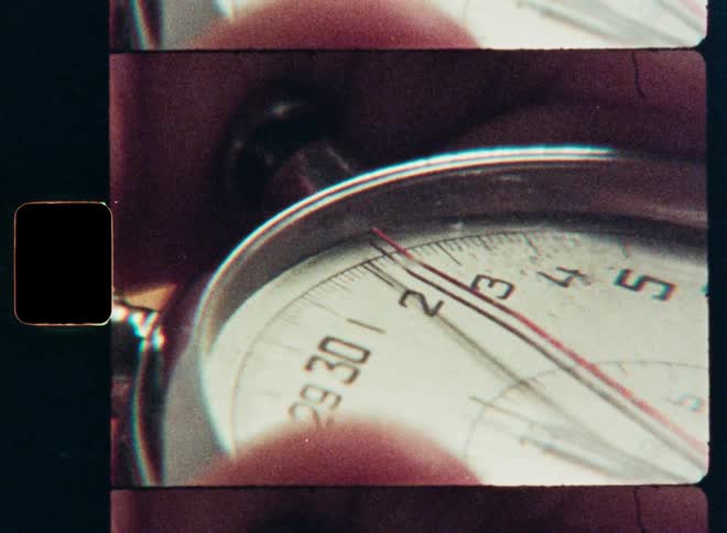 A vintage Super 8 film scan shows a macro close-up of a stopwatch counting time