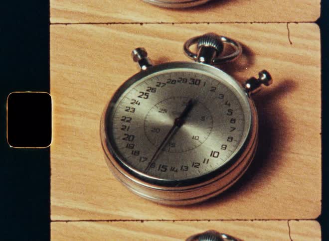 A vintage mechanical stopwatch with a sweeping second hand ticks away the seconds in a close-up shot with visible film sprockets