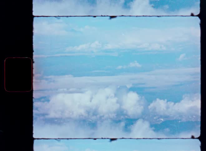A vintage Super 8 film scan shows a serene aerial view of fluffy white clouds in a bright blue sky