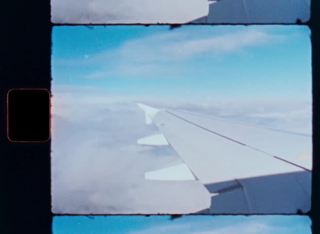 Vintage Super 8 film captures the view of an airplane wing flying high above a sea of clouds on a sunny day