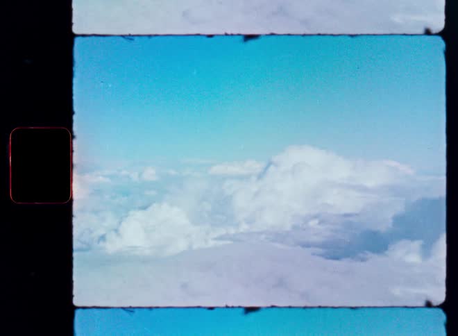 A vintage film scan shows a dreamy view of the clouds and blue sky from an airplane window