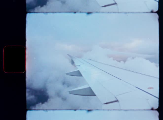 A nostalgic view from an airplane window shows the wing gliding through dense clouds, captured on vintage film