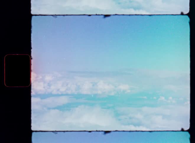 A vintage 8mm film captures an aerial view of fluffy white clouds drifting across a serene blue sky