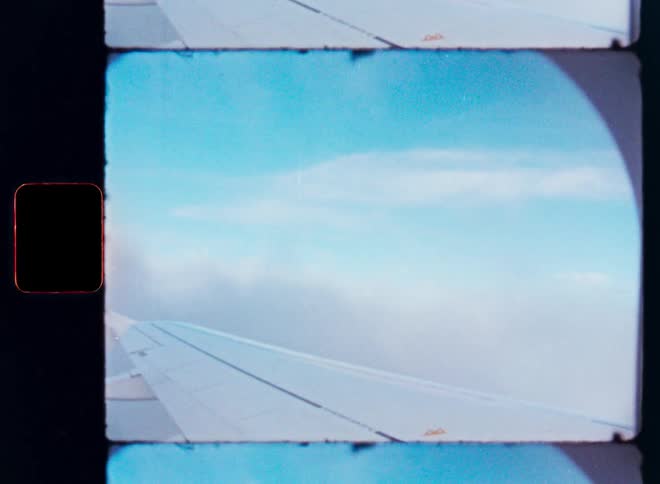 A nostalgic view from an airplane window, shot on Super 8 film, shows the wing flying through the clouds