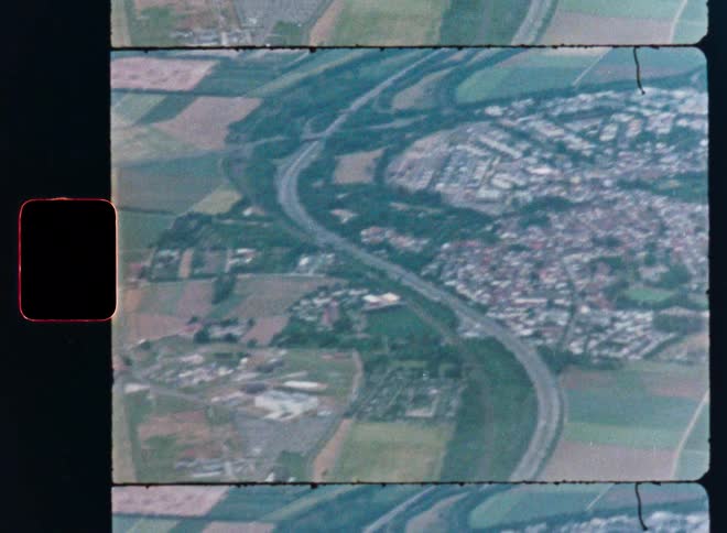 Vintage 8mm film scan shows an aerial view of a highway winding past a small town and through the countryside