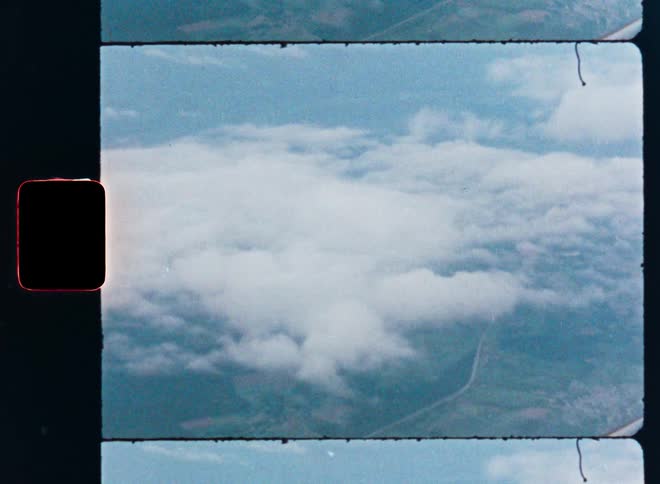A vintage film scan captures an aerial view of fluffy white clouds over a green landscape below