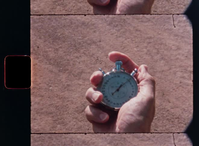 Vintage Super 8mm footage captures a close-up of a hand clicking a stopwatch at a track and field event