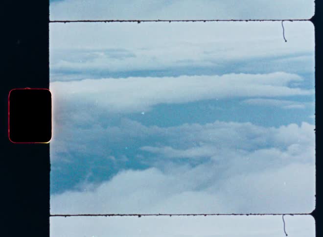 An archival film scan captures a serene aerial view of clouds floating in the blue sky