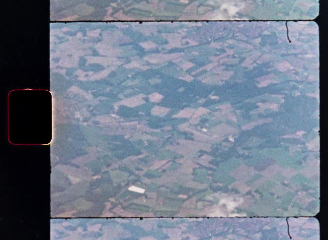 A vintage 8mm film scan captures a top-down aerial view of a sprawling patchwork of green countryside fields