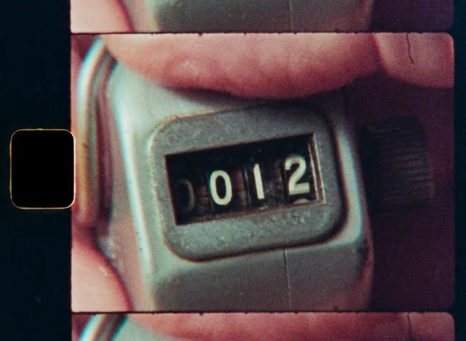 Super 8 film style close-up of a hand clicking a metal tally counter, with the numbers increasing sequentially