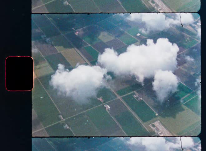 Vintage archival film captures a high-angle aerial view of fluffy white clouds floating over geometric green farm fields
