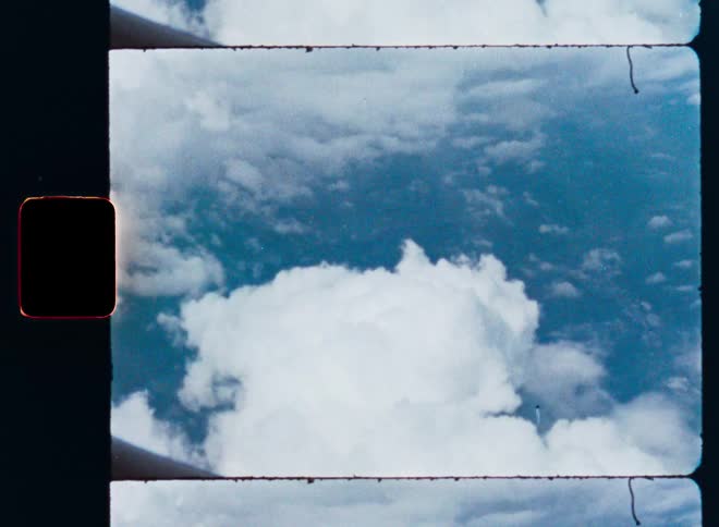 An aerial view of puffy white clouds against a blue sky, captured on grainy vintage film with a visible film strip border