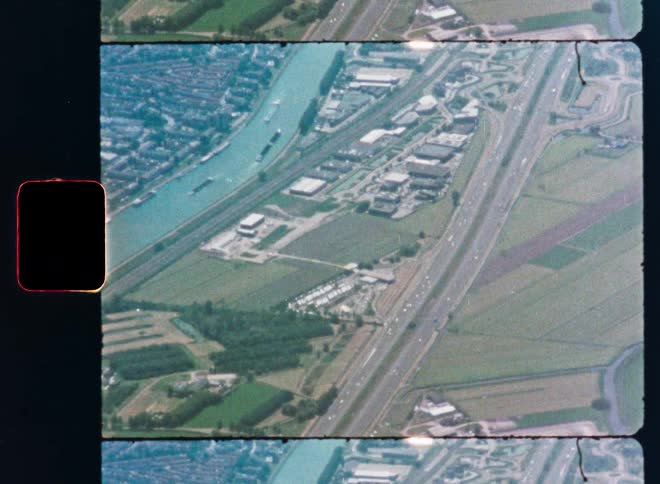 A vintage film scan captures a high-angle aerial view of a city with a river and a busy highway