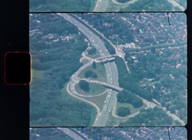 Vintage 8mm film captures a stunning aerial view of a bustling highway interchange cutting through a green, wooded landscape