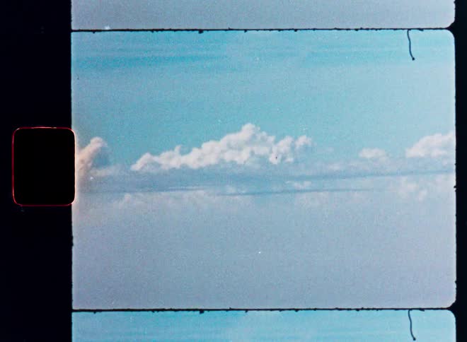 An authentic 8mm film scan capturing a serene aerial view of white clouds in a vast blue sky