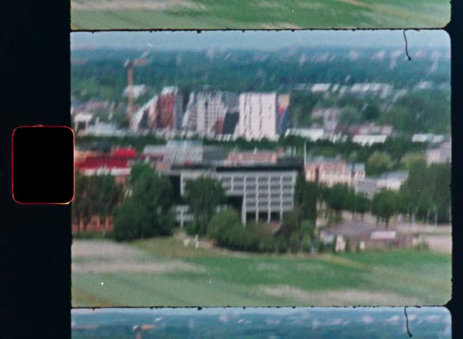 A shaky, high-angle view of a city with modern buildings and green spaces, shot on vintage film