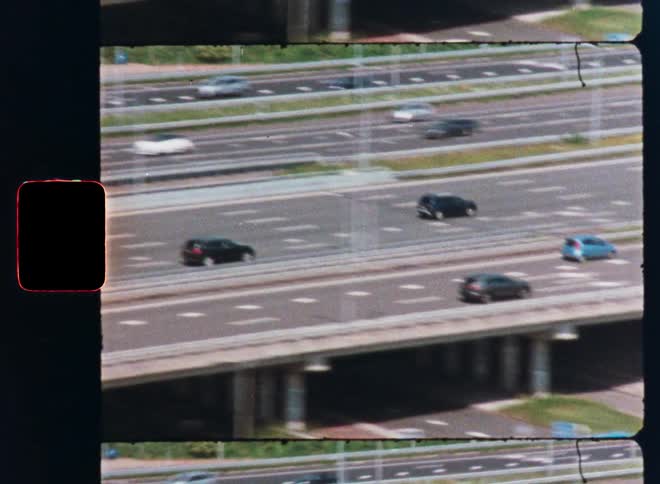 A vintage film perspective from a moving vehicle captures traffic flowing along a busy urban highway