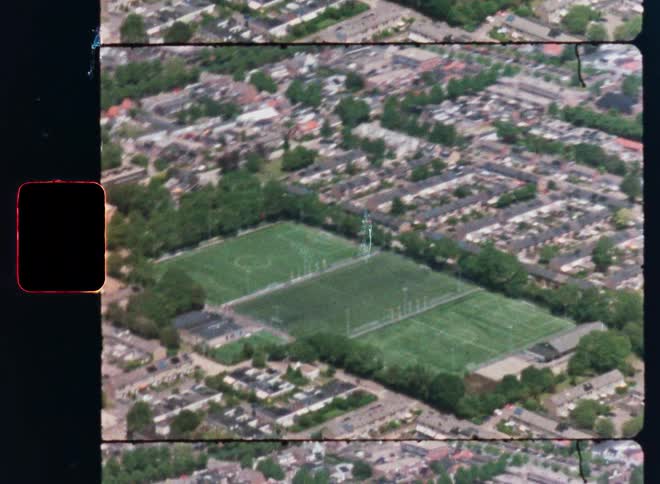 Vintage 8mm aerial footage captures a bird's-eye view of lush green soccer fields nestled within a residential neighborhood