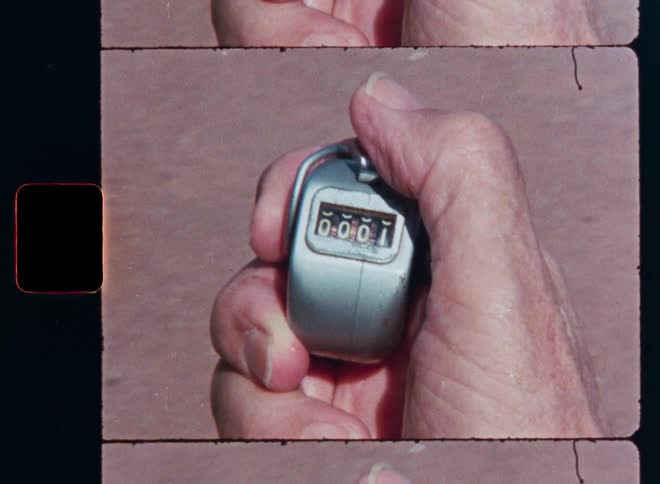 A close-up of a hand clicking a mechanical tally counter from zero to one, captured on vintage film
