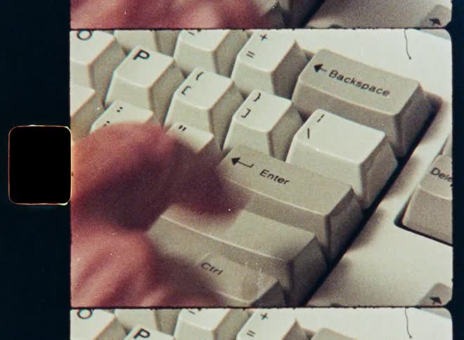 Vintage 8mm film captures a close-up of a hand pressing keys on an old-school computer keyboard