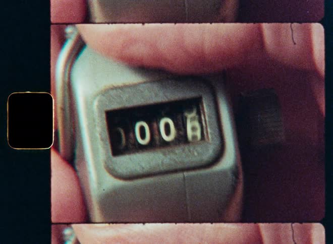 An extreme close-up shot on vintage film of a hand using a metal tally counter to count upwards from zero to eleven