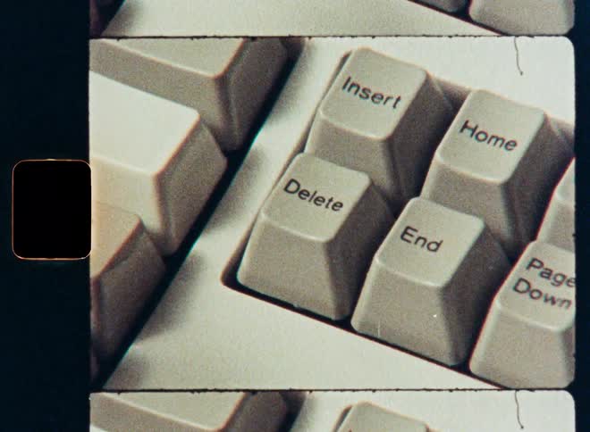 Vintage film close up of a finger pressing the delete key on a retro computer keyboard