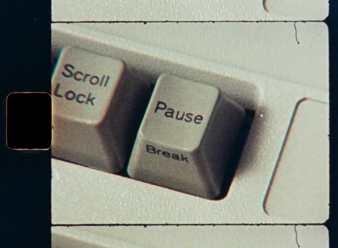 A retro film-style close-up of a finger pressing the Pause/Break key on a vintage computer keyboard