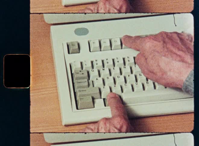 A person's hands type on an old computer keyboard in this overhead shot with a retro film look