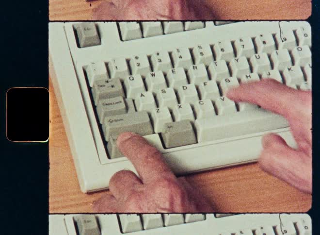 Close up of hands typing on a vintage personal computer keyboard in an 8mm film style