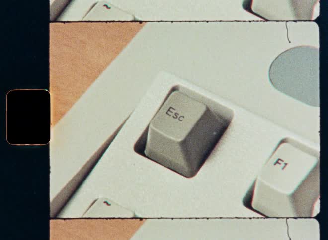 A close-up shot of a finger pressing the 'Esc' key on a vintage computer keyboard with a retro film look