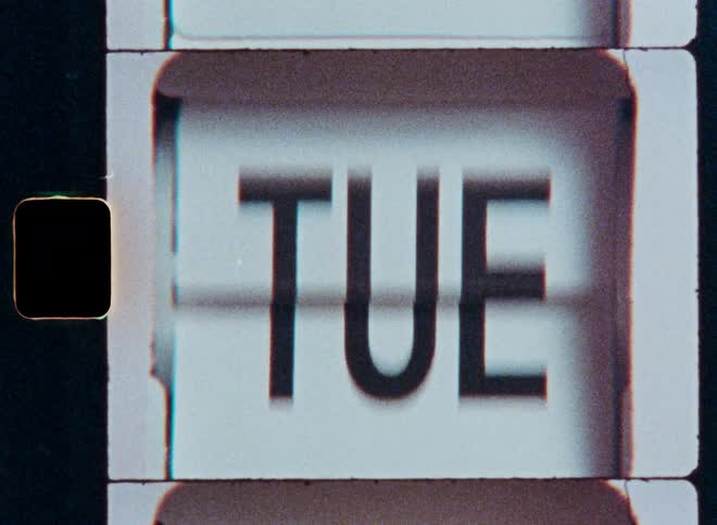 The days of the week flip by on an old mechanical calendar, shot on grainy vintage film