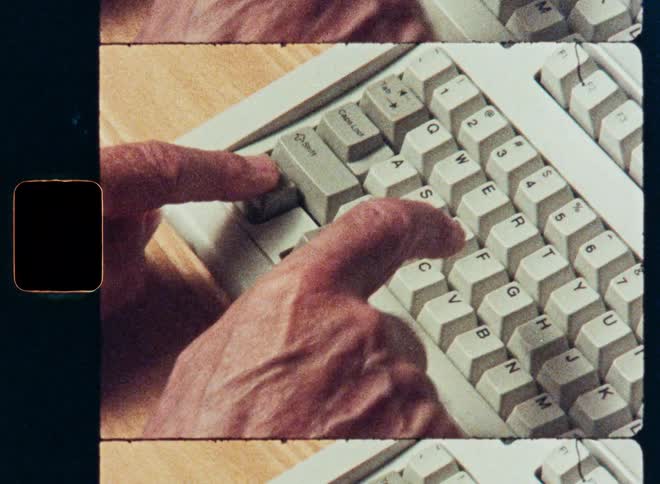 Close-up of hands typing on a retro computer keyboard on a wooden desk, with an 8mm film aesthetic