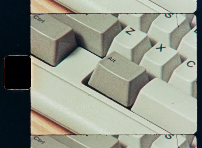 Close-up of a finger pressing the 'Alt' and 'X' keys on a vintage PC keyboard with a retro film strip effect