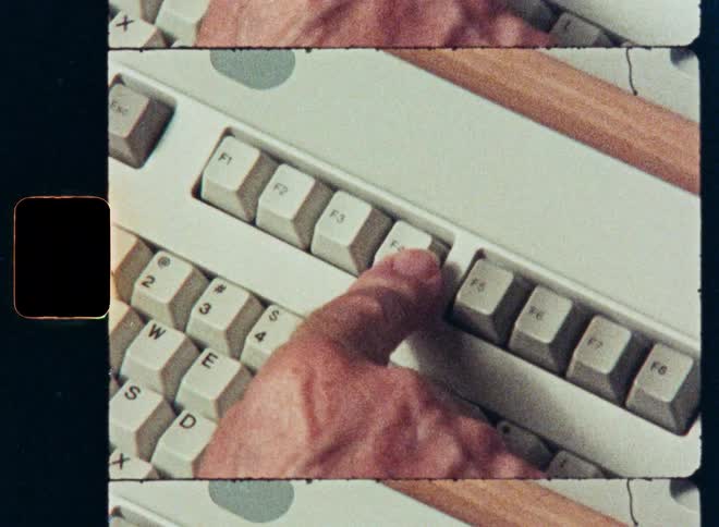 A close-up of a finger pressing keys on a vintage computer keyboard with a retro film strip aesthetic