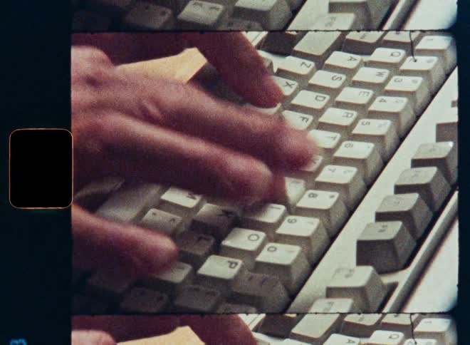 A close-up of hands typing on a vintage computer keyboard with an 8mm film effect
