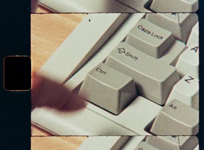 Vintage film footage shows a close-up of a finger pressing the shift key on a retro computer keyboard