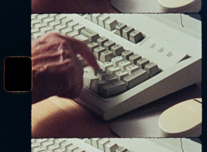 Vintage film scan captures a close-up of a hand typing on the number pad of an old computer keyboard