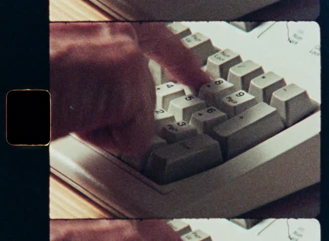 Vintage archival footage shows a close-up of a person's hand typing on an old computer keyboard's number pad