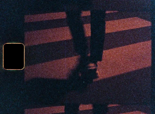 Grainy super 8mm footage shows the shadow of a couple holding hands while walking across a striped crosswalk