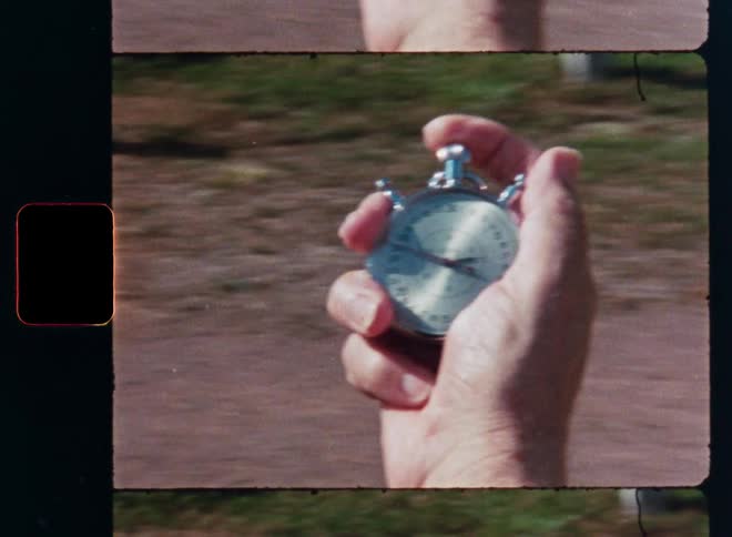 Vintage film captures a close-up of a hand starting and stopping a mechanical stopwatch while running on a dirt track
