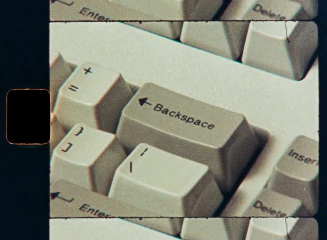 A close-up shot of a finger repeatedly pressing the backspace key on a vintage computer keyboard, filmed with a retro film effect