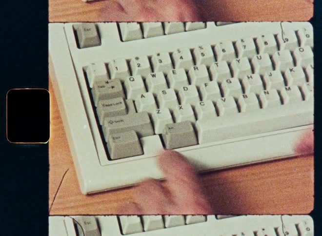 A close-up of hands typing on a vintage computer keyboard in an 8mm film aesthetic