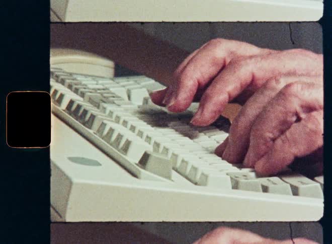 A grainy close-up shot captures hands typing on an old-school computer keyboard, evoking a sense of nostalgia